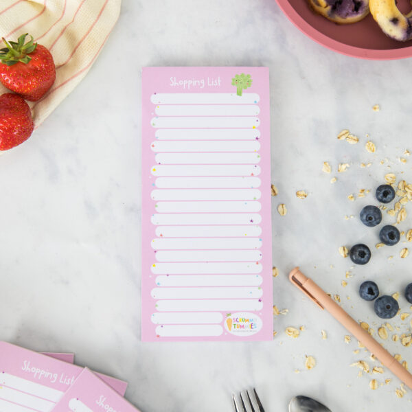 a pink a white shopping list pad surrounded by oats, blueberries and strawberries.